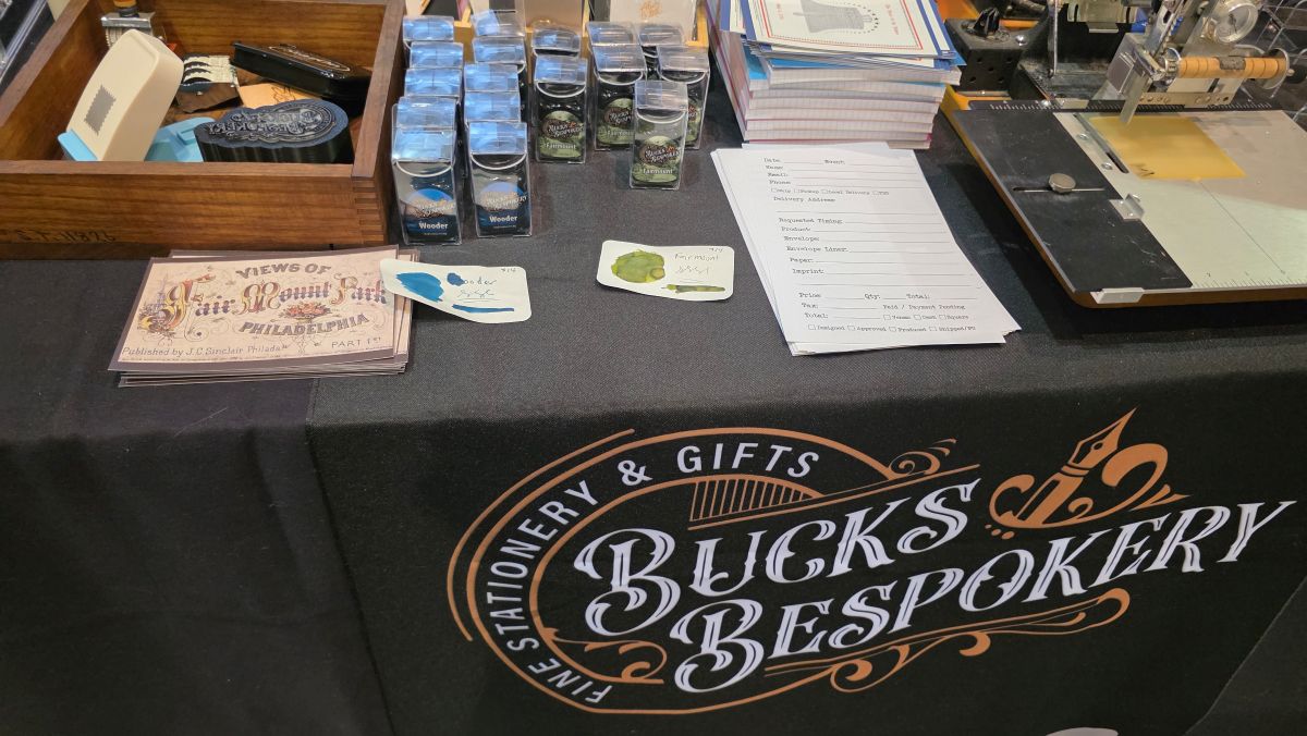 The Bucks Bespokery table with their custom inks, postcards, and stamps and a hot press people could use to stamp their paper or notebooks.