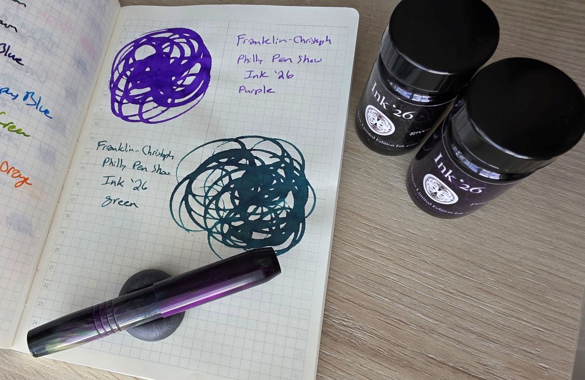 Swirled swatches of the vibrant purple and green Philly Pen Show '26 inks from Franklin-Christoph next to the glass bottles of ink and a matching pocket size pen.