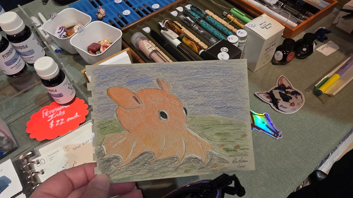 Orange dumbo octopus drawn by Inkdependence Mike with colored pencils on gray paper.