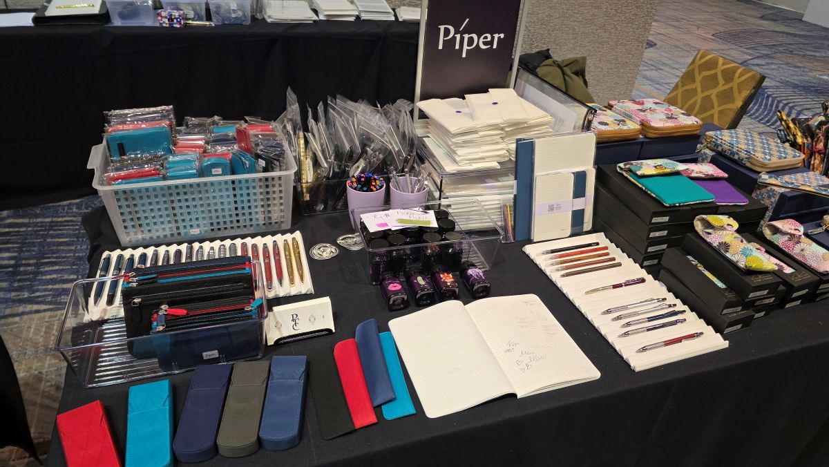 The Piper Trading Co table with colorful pen cases and pouches, four inks, paper, and standard pens and mechanical pencils.