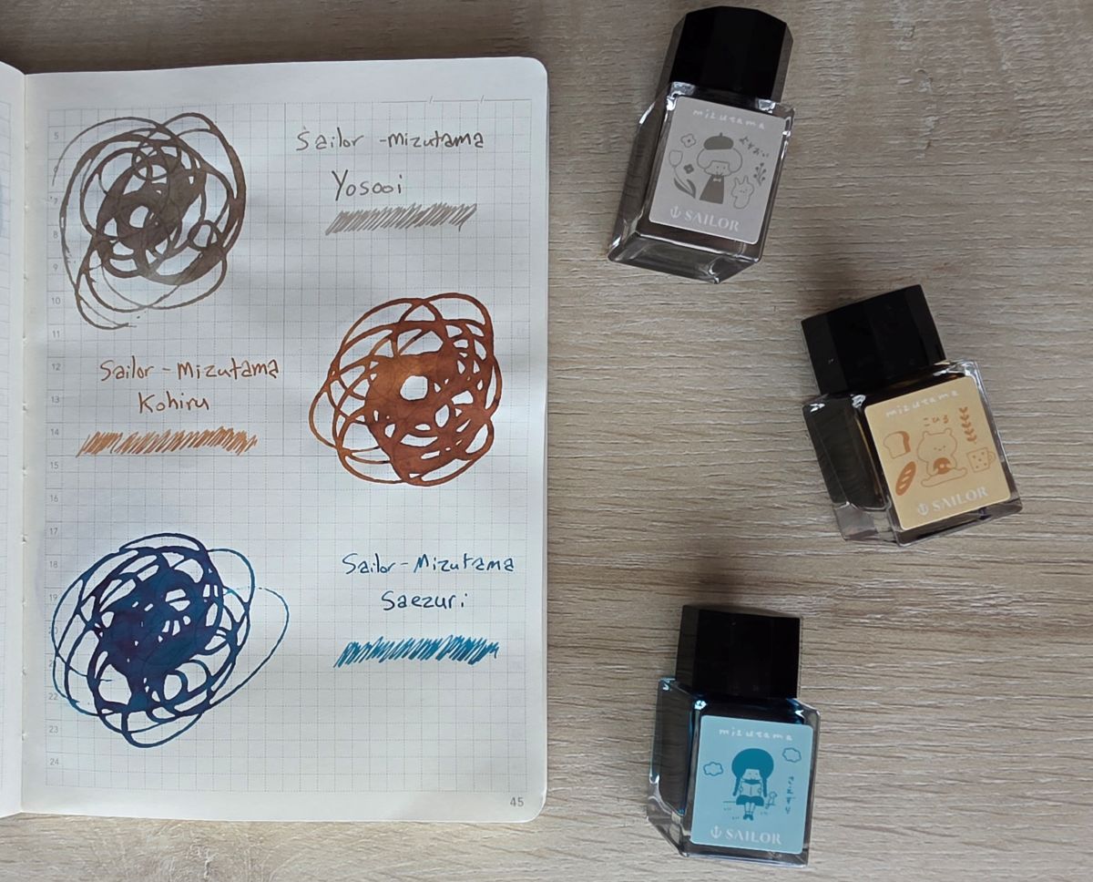 Ink swatches and glass ink bottles for three Sailor Mizutama inks including a gray brown called Yosooi, an orangy-brown called Kohiru, and a slightly green-leaning blue called Saezuri.