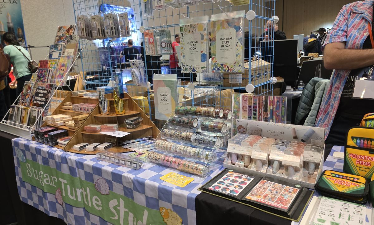 The Sugar Turtle Studio table at the pen show filled with notebooks, stamps, washi, stickers, pencils, pen cups, Rickshaw Bags, and more.