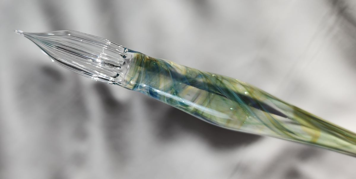 Closeup of glass dip pen with green and blue swirls through clear glass with sparkles