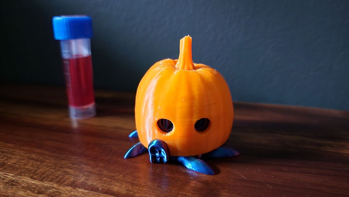 3D printed multicolor octopus ink vial holder wearing a pumpkin costume, sample ink vial in background.