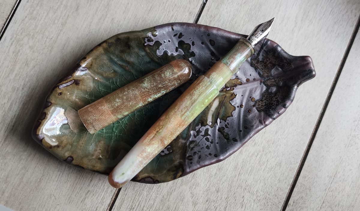 Turned acrylic fountain pen in a translucent peachy brown with green sparkles and swirl of white