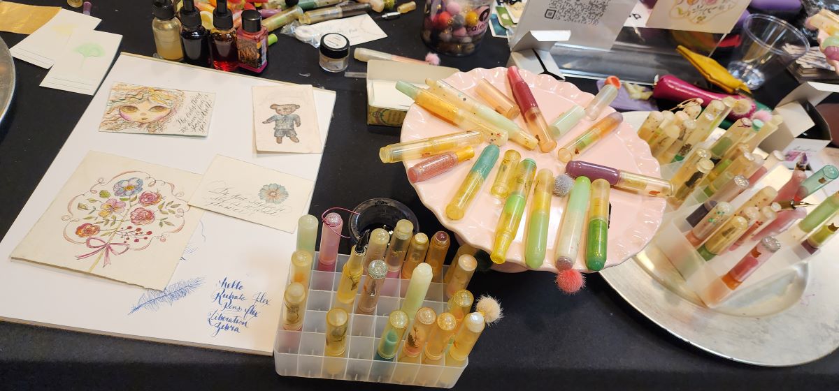 Rubato Pens table with many colorful pens, delicate sketches, and supplies.