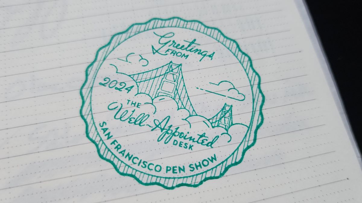 Teal blue stamp on notebook page that says Greetings from San Francisco Pen Show 2024, The Well-Appointed Desk, with the Golden Gate Bridge