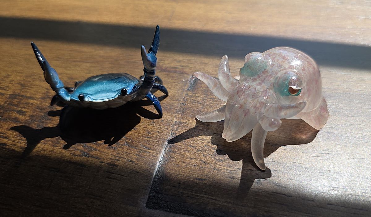 A small blue-black crab pen holder and a translucent white and pink cuttlefish pen holder.