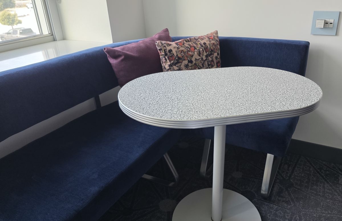 A small oval table next to a curved couch with some throw pillows in a hotel room.