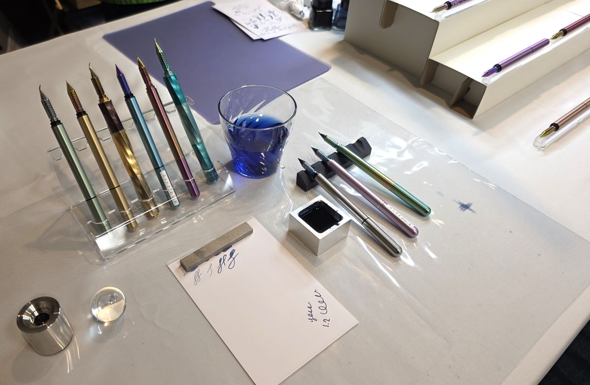 Nine metal Drillog dip nib test pens with test paper, metal ink well, and rinse water.