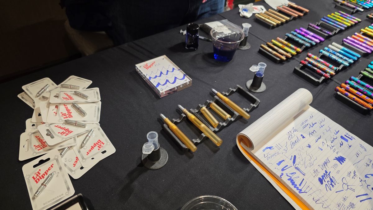 The Schon DSGN table with demo pens of the Lil' Dipper metal dip pen nib with multiple colors of Pocket Six pens visible in the background.