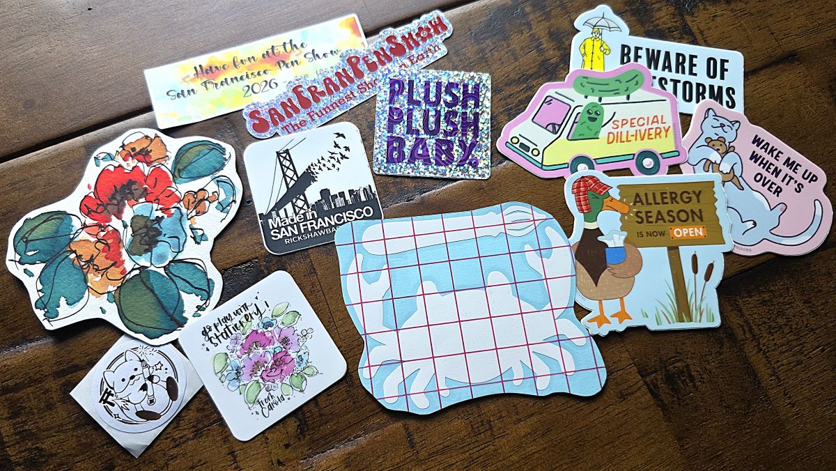 A mix of stickers and a floral ink painting spread out on a desk.