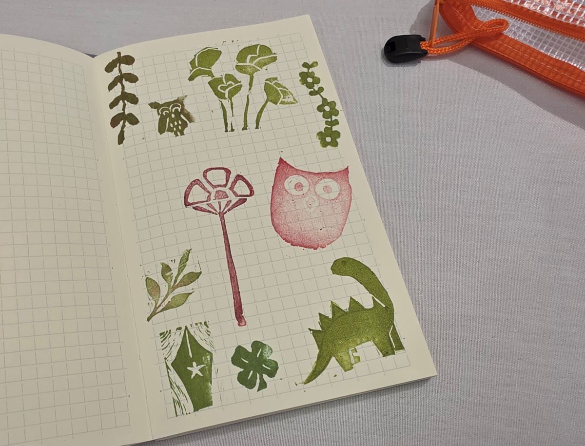 Notebook with stamps of flowers, owls, leaves, a pen nib, and a dinosaur.