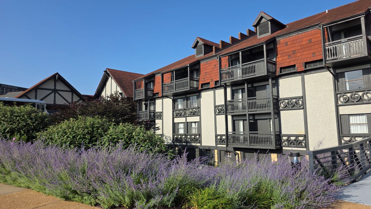 The front portico and four-story wing of the Sheraton Westport Chalet Hotel with red roof, off white walls and dark trim and beams in the style of a chalet.