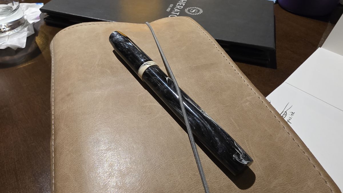A Franklin-Christoph Model 45 in a dark black material with swirls of pearlescent shimmer and cream tucked into the elastic of a B6 Roterfaden.