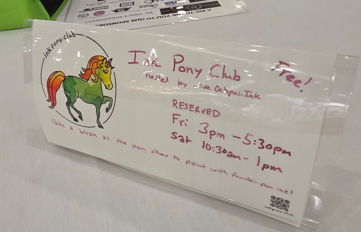 Laminated table sign with details of the times for Ink Pony Club and an example painted pony.