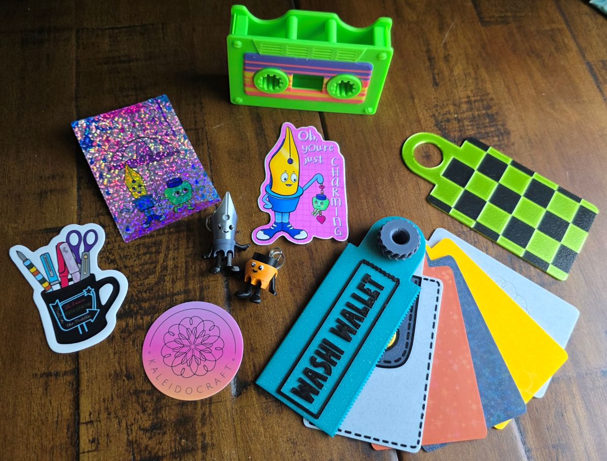Several 3D printed items including a cassette tape washi holder, ring of washi storage cards, pen nib and ink bottle charms and several stickers.