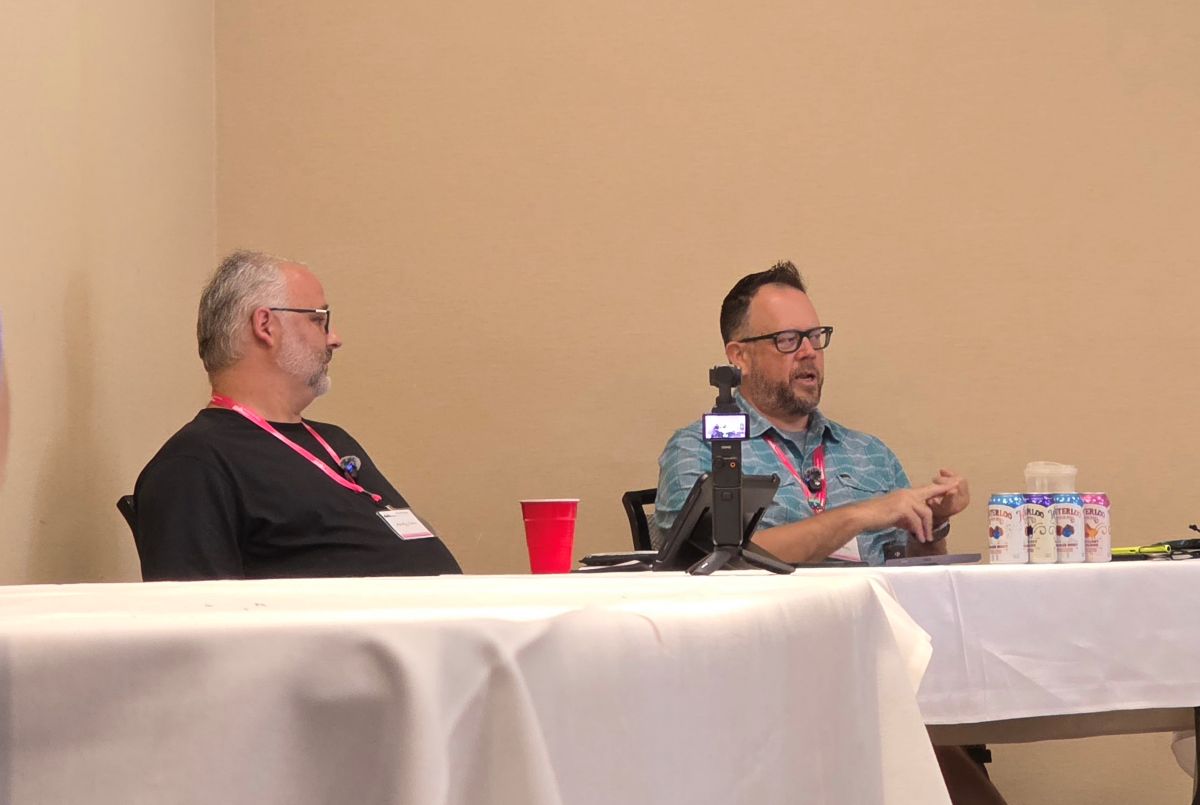 Andy and Brad sitting behind a table at the panel while Brad answers questions.