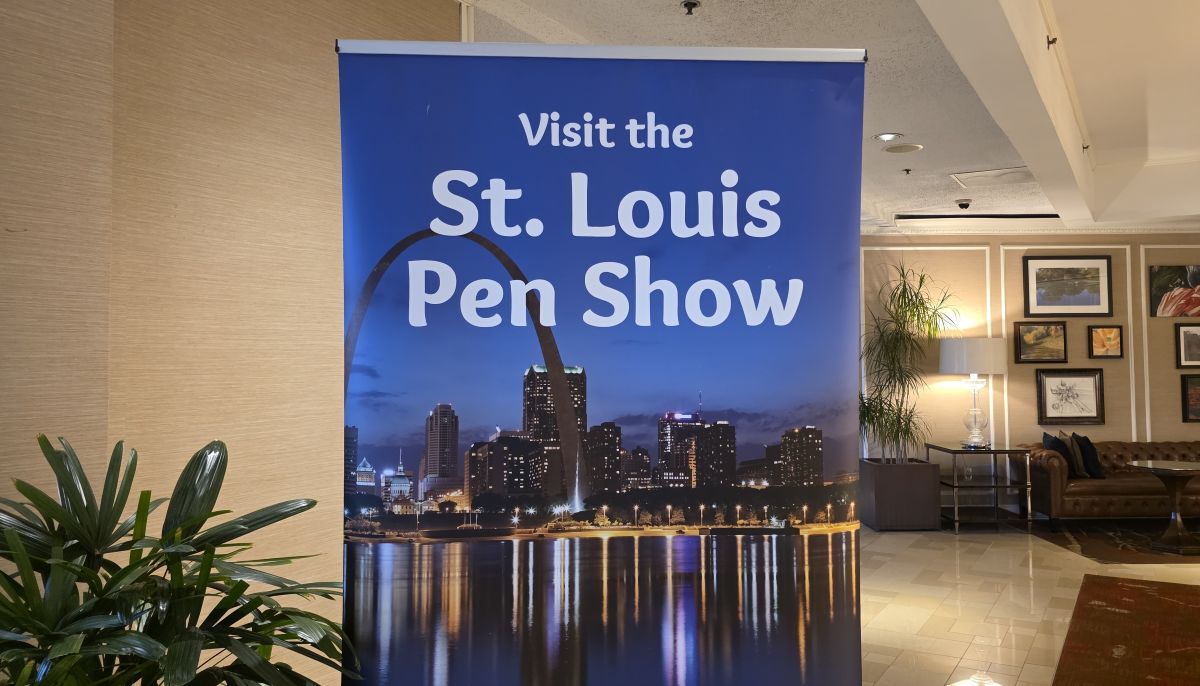 Sign with photo of St. Louis arch and skyline at dusk with the text Visit the St. Louis Pen Show.