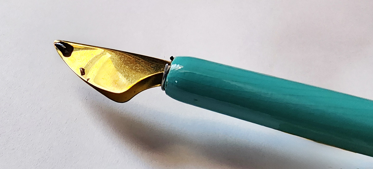 A metal nib with two edges folded together to make a curved shape pointed at the tip and curving to a wide base and an ink channel in between.