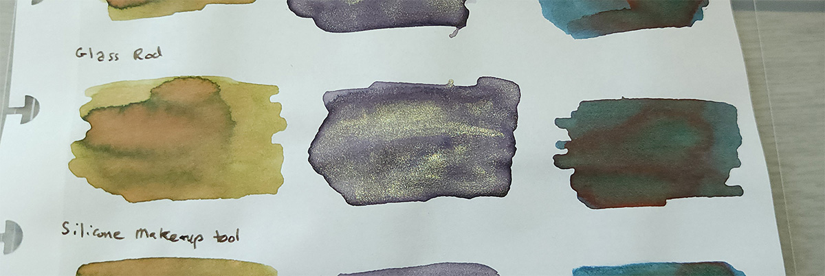 Ink swatches of Sailor 280 with a pale green and areas of a pinkish hue with dark edges, Colorverse Iris Nebula with dark edges and heavy champagne color shimmer, and Taccia Sabimidori with shading blues and greens and lines of red sheen winding through the swatch.