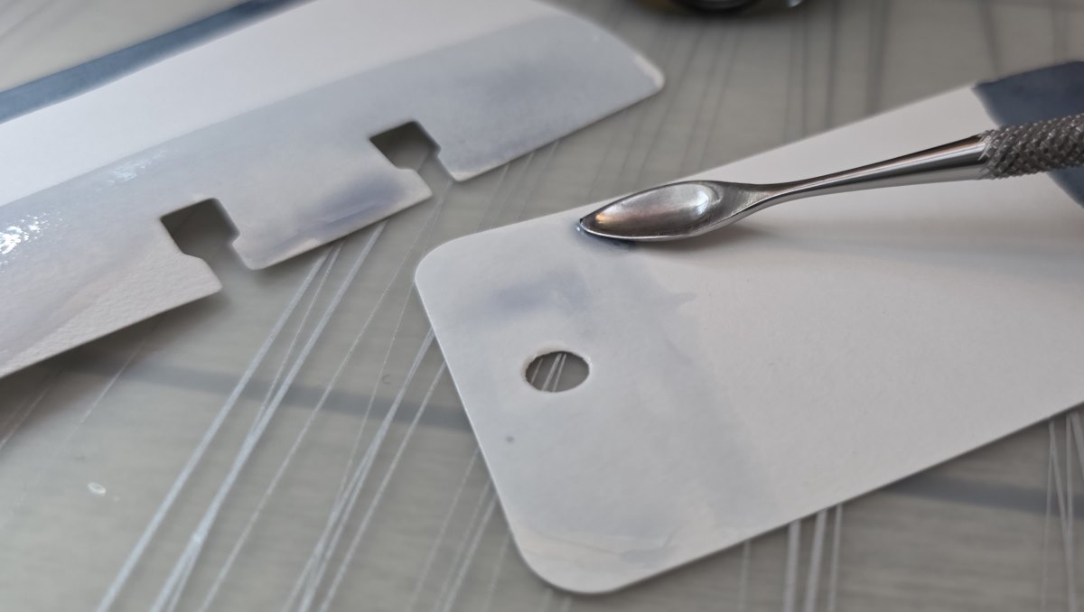 Close up of a small metal carving tool shaped like a spoon spreading ink diluted in water along one side of the Col-o-ring card.