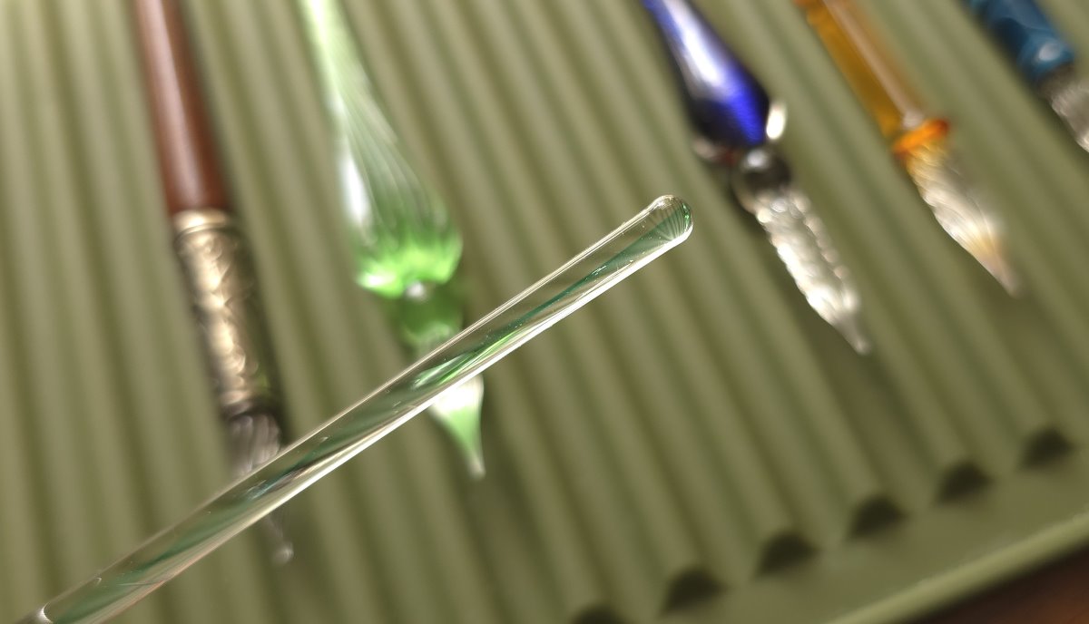 Close up of the handle of a glass dip pen that has a smooth round end like a glass stir rod.