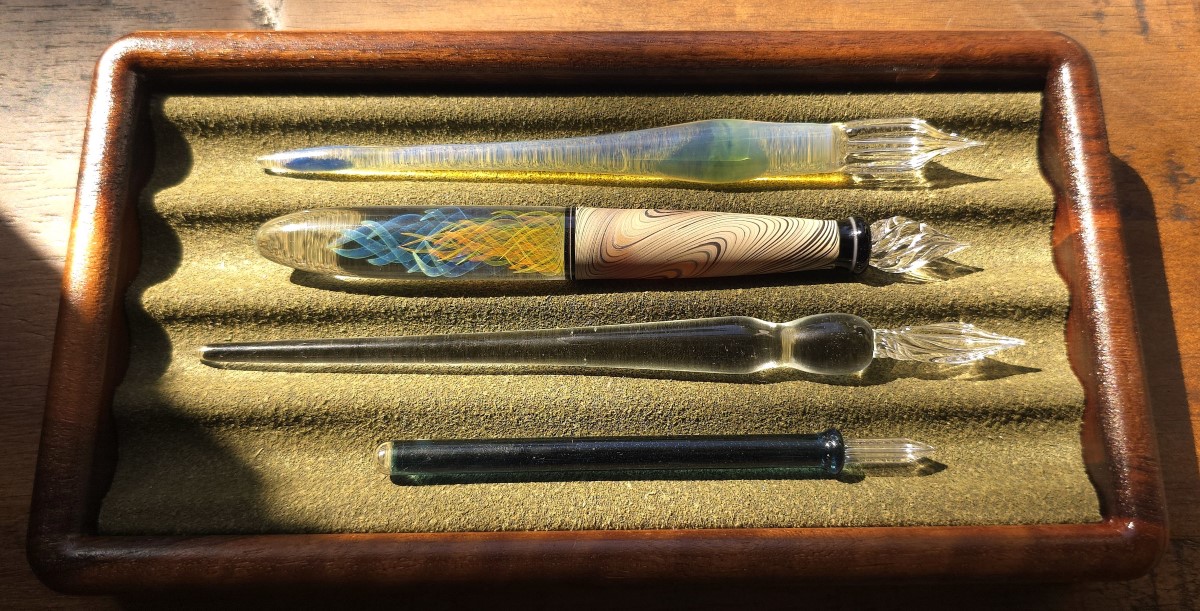 Four Japanese glass dip pens from Glass Studio AUN, Hanabi Glass Studio, Takeda Mio, and Kemmy's Labo in a dark olive green pen tray.