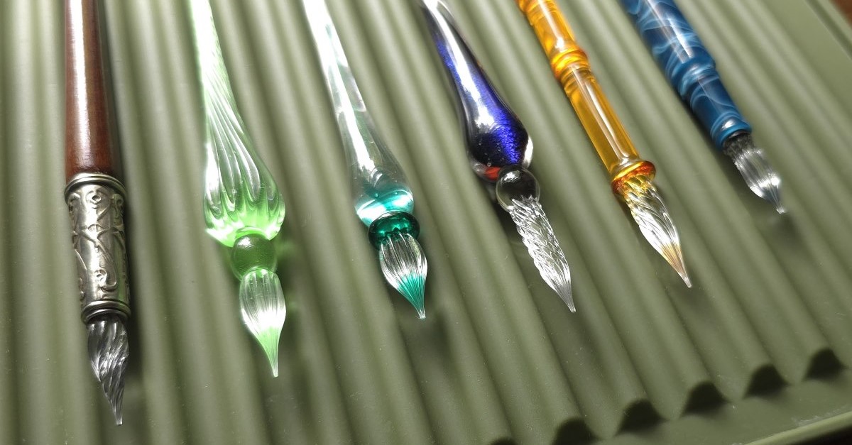 A green silicone drying mat with six glass pens of different sizes, shapes, and colors.
