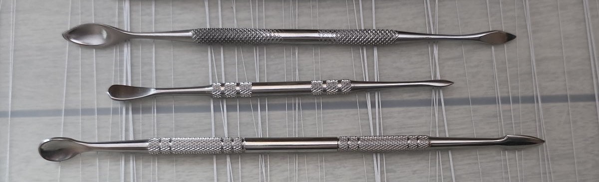 A group of three metal tools with a small spoon shape on one end, one a bit shorter and less spoon-shaped than the other two.
