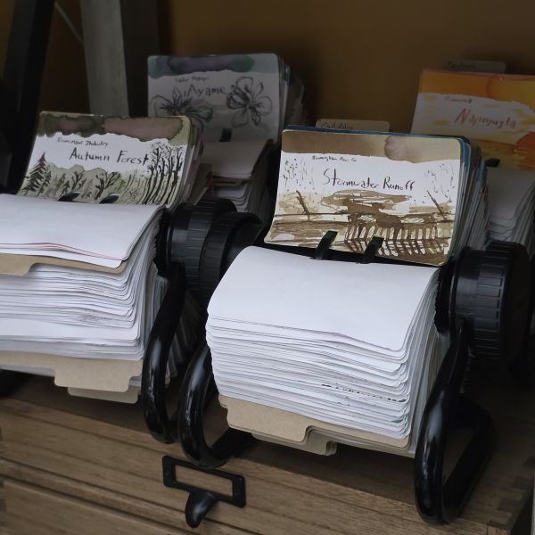 Four circular Rol-o-dex holders on a shelf, each filled with Col-o-dex cards with ink swatches and sketches.