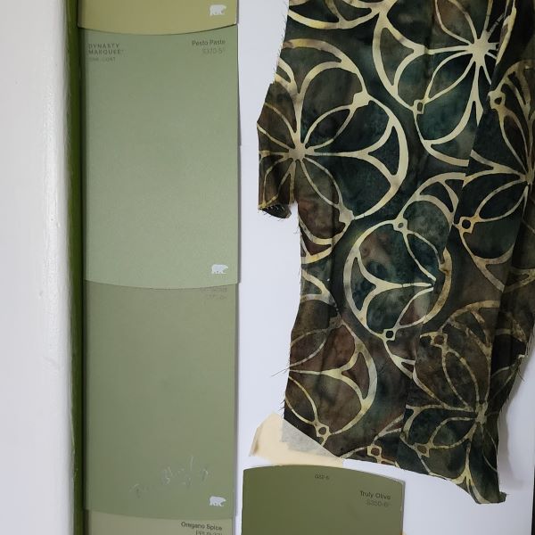 A scrap of dark green batik fabric and multiple green wall paint swatches hung on a white wall.