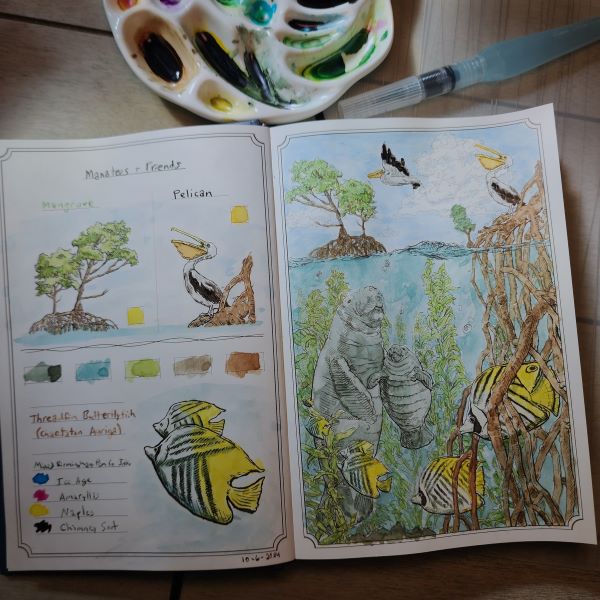 Open book showing a painted scene of manatees under water with bright yellow fish, trees with large roots under water, seaweed, and pelicans. Next to the book is a water brush and a ceramic paint palette filled with different colors of ink, everything is on a desk in a beam of sunlight.