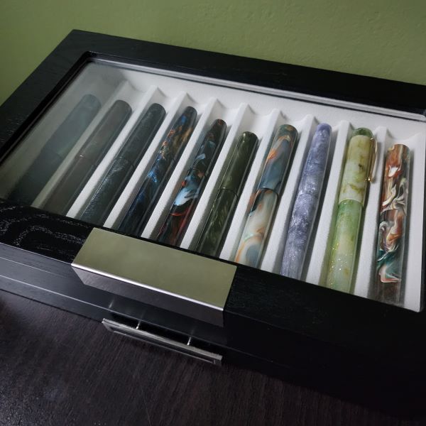 A wood pen storage box with 10 fountain pens visible through the glass lid.