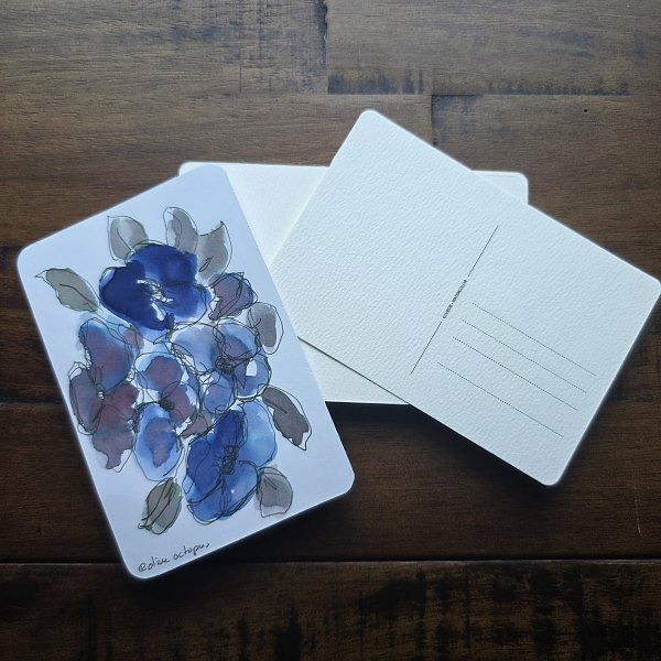 Painted floral design on a postcard next to pile of blank watercolor postcards.