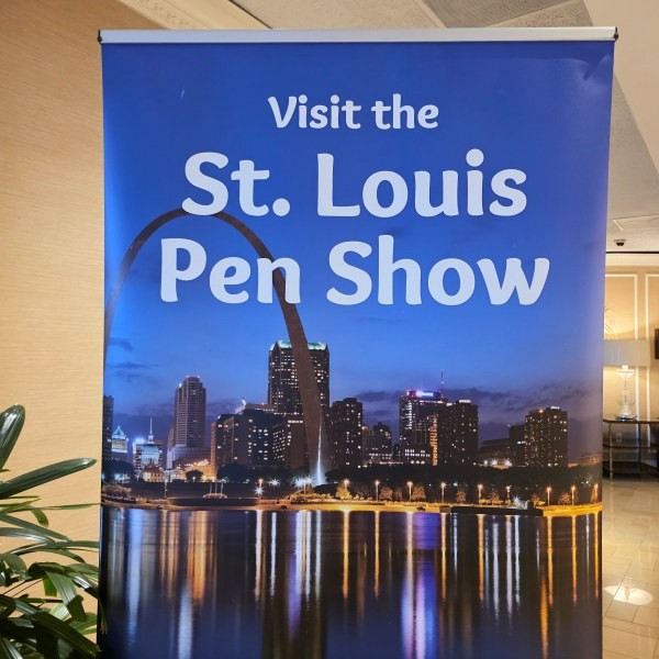 Sign with photo of St. Louis arch and skyline at dusk with the text Visit the St. Louis Pen Show.