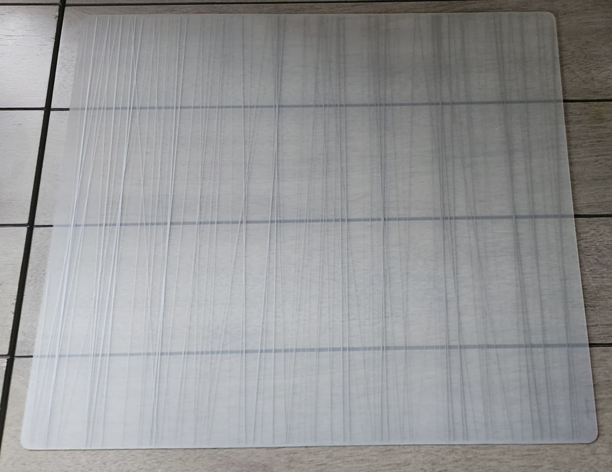 A translucent white silicone placemat with a simple design of thin, vertical lines in a matte metallic silver, sitting on a gray wood desk.