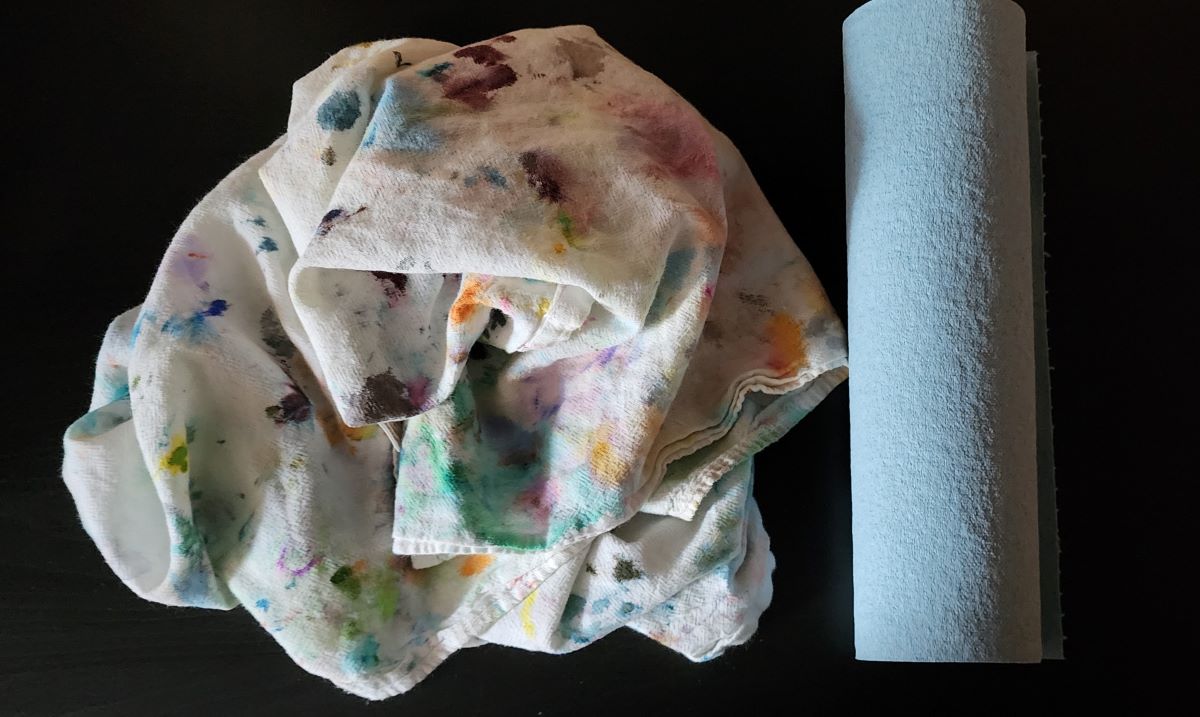 A white flour sack towel covered in ink stains and a roll of disposable blue shop towels.